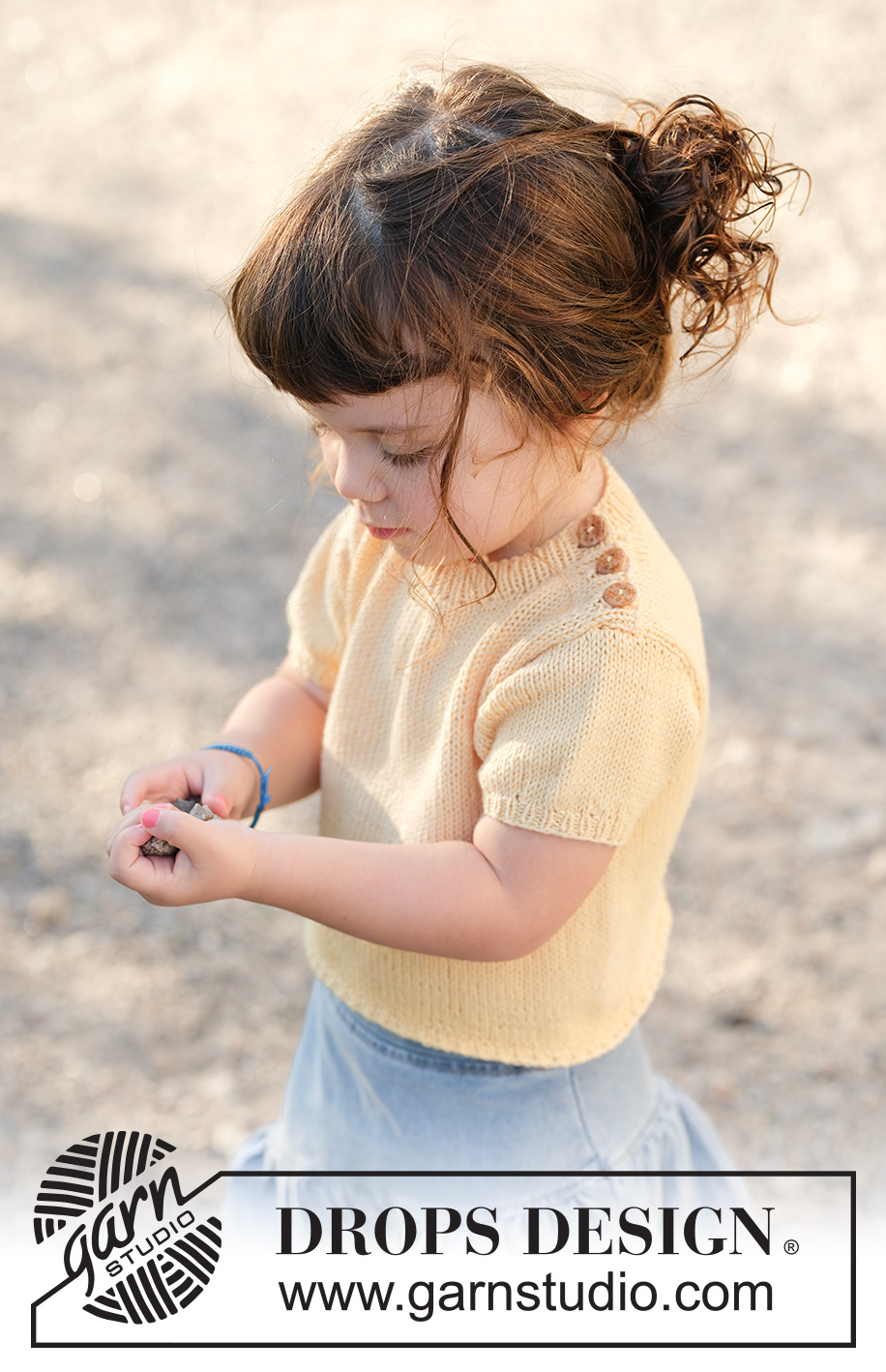 Sunshine Sprout / DROPS Children 49-3 - Jersey de punto para niños en DROPS Cotton Merino. La pieza está tejida de abajo hacia arriba con mangas cortas y borde para botones sobre el hombro. Tallas 2 – 12 años.